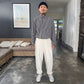 Man standing in a modern living room wearing a checkered shirt, white pants, and a beanie.